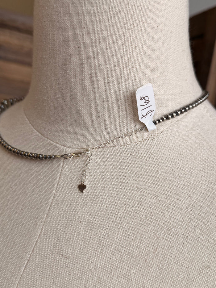 Sterling silver graduated bead necklace with small charm drop and brand tag at collar