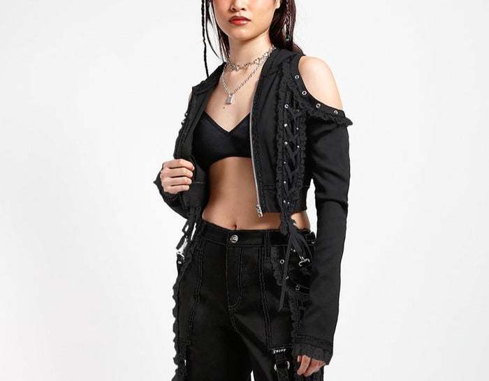 front of Black hoodie with gothic Lolita details. Hoodie has long sleeves that have thumb holes and black lace around the hands. Shoulders are open, and have edges of black on black lace details, as well as silver rivet details around the edge. Front of hoodie zips up, and has black on black lacey lace-up panels on right and left of zipper. Hoodie has black hood.