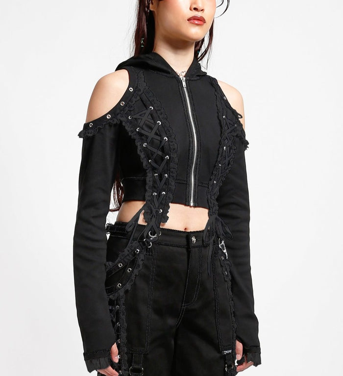 side of Black hoodie with gothic Lolita details. Hoodie has long sleeves that have thumb holes and black lace around the hands. Shoulders are open, and have edges of black on black lace details, as well as silver rivet details around the edge. Front of hoodie zips up, and has black on black lacey lace-up panels on right and left of zipper. Hoodie has black hood.