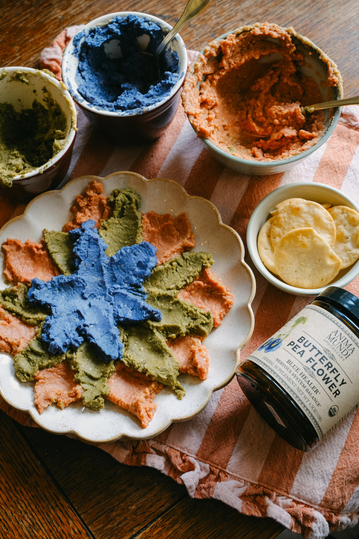 Assorted dips and spreads on a wooden table with a jar of butterfly pea flower paste.