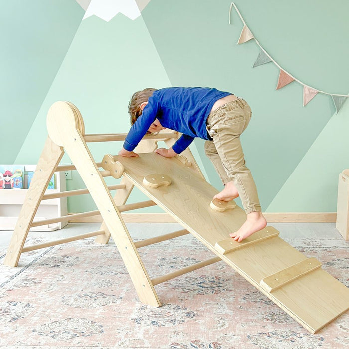 Toddler climbing through a wooden montessori climber using his foot to step on each peg or hold and wooden slat bar from Sapiens Child