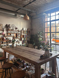 Cozy cafe interior with wooden tables, shelves, and large windows.
