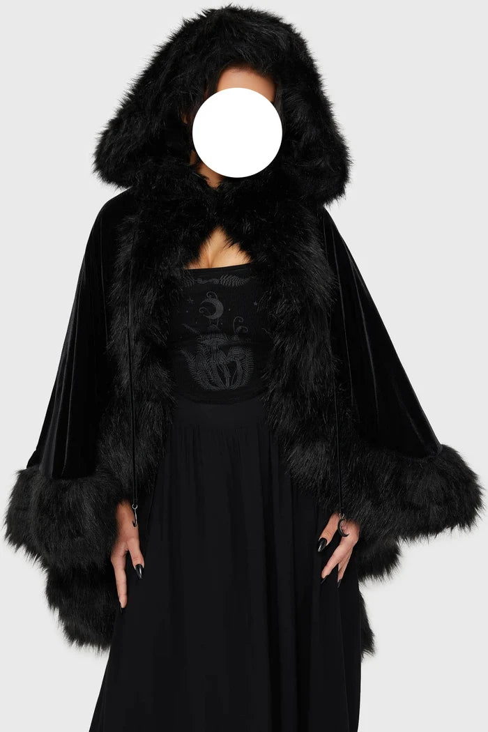 Model wearing a black faux fur-trimmed hooded cloak over a black dress on a white background