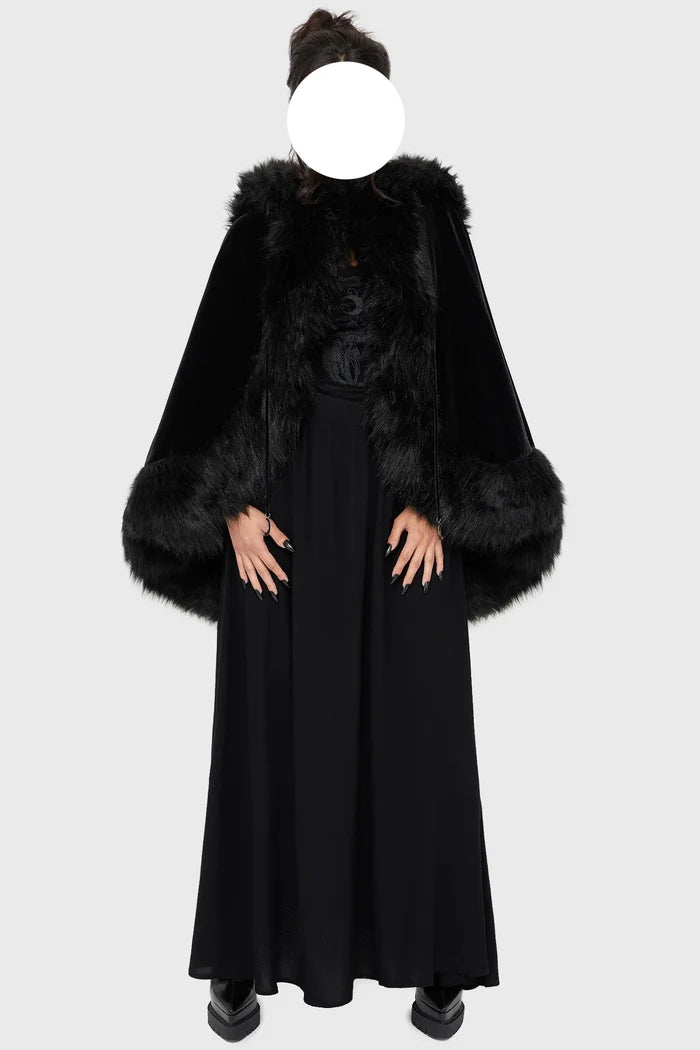 Model wearing a black faux fur-trimmed hooded cloak over a black dress on a white background