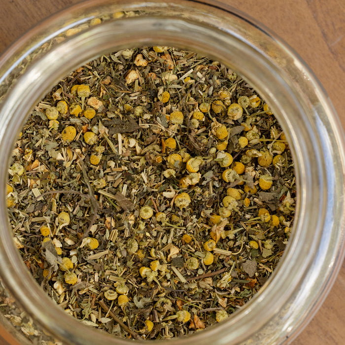 Close-up of a glass jar filled with dried herbs and flowers on a wooden surface.