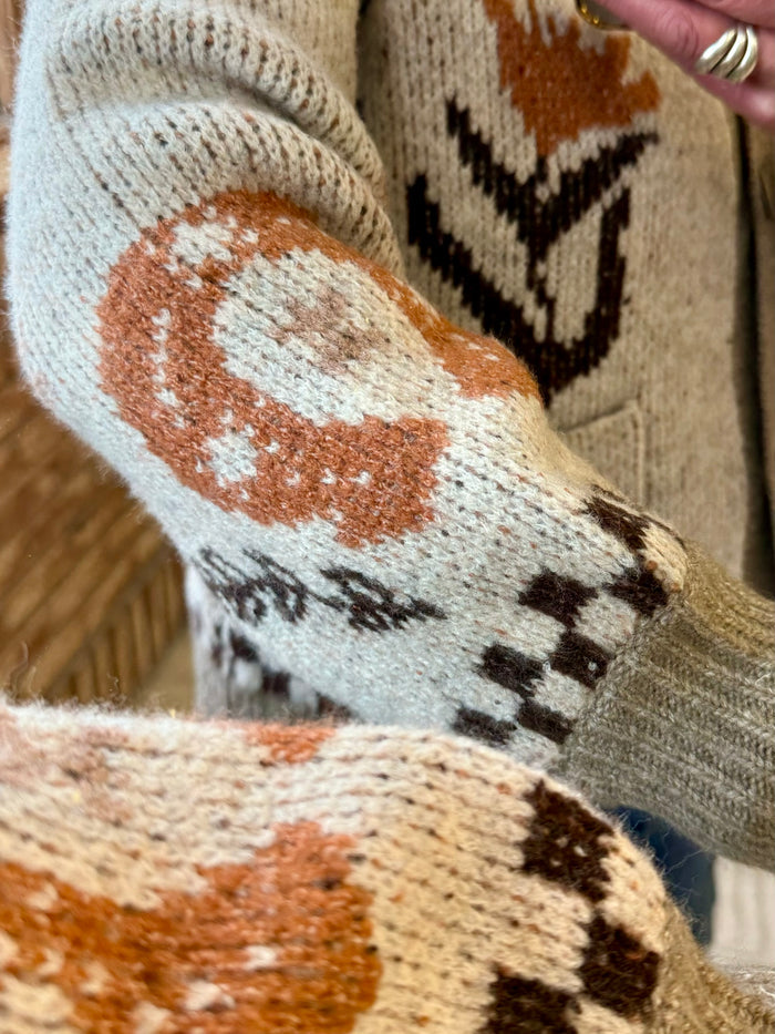 Sleeve detail of taupe knit cardigan with orange swirl and black leaf pattern