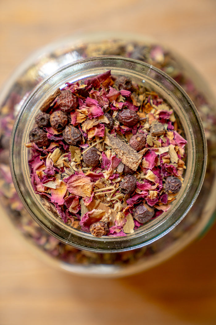 Close-up of a glass jar filled with dried flowers and herbs on a wooden surface.