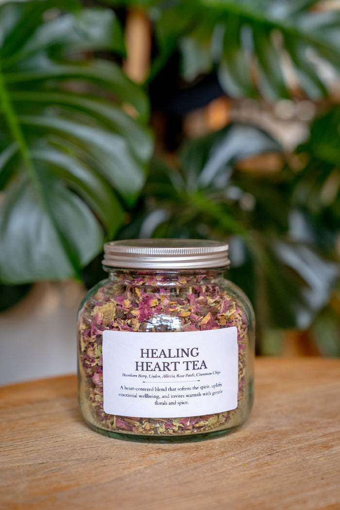 Jar of 'Healing Heart Tea' with a label on a wooden surface, plant in the background