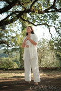 Woman in white outfit standing under a tree with a natural background