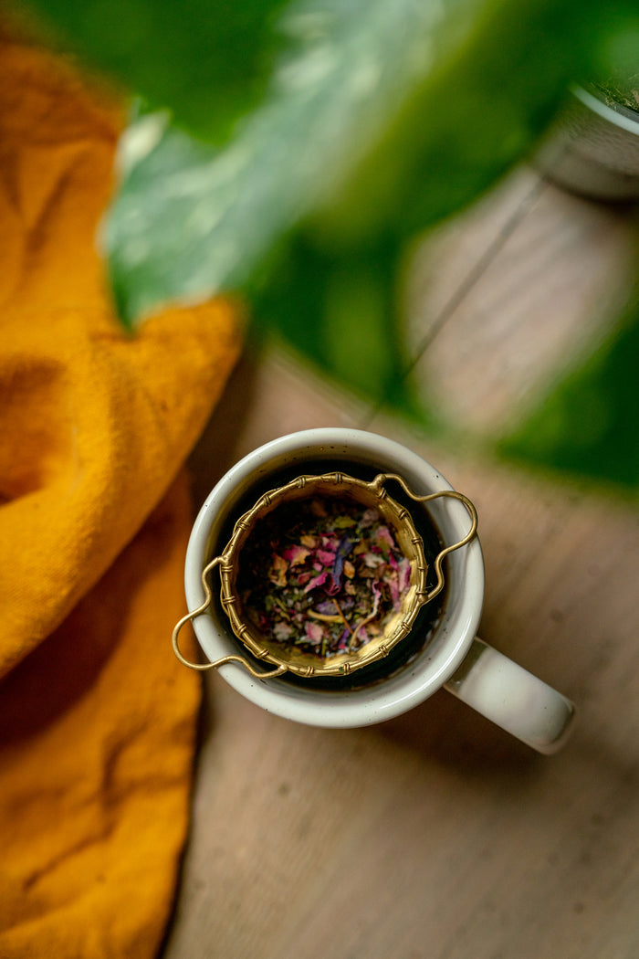 Tea infuser with loose tea leaves in a white mug on a wooden surface.