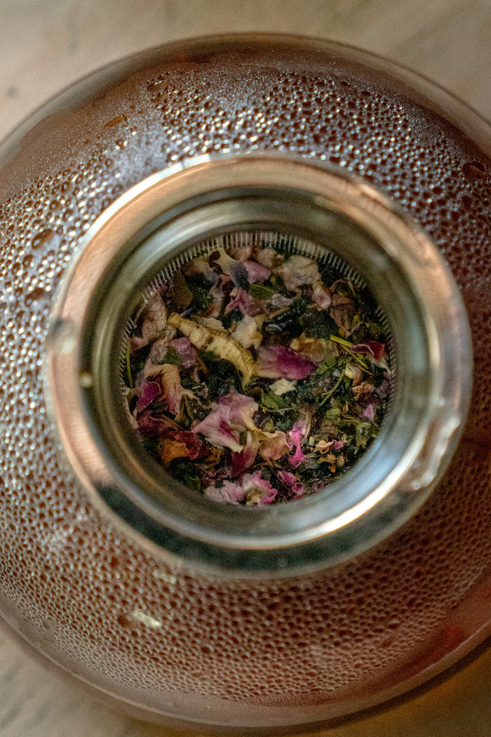 Tea strainer with dried tea leaves and flowers inside a glass container.