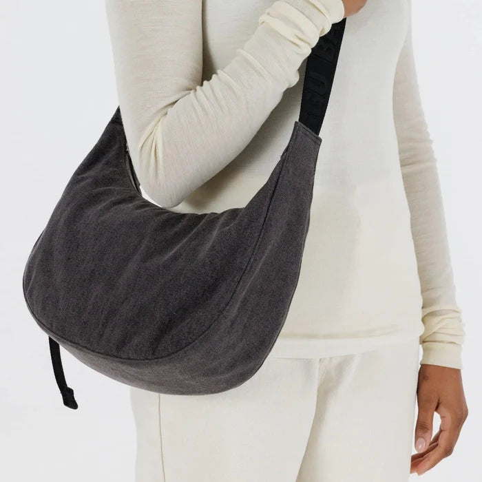Person holding a black denim shoulder bag against a white background
