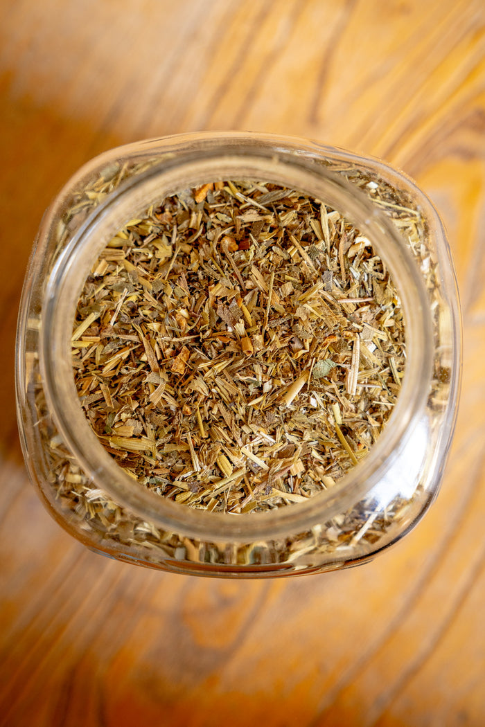 Glass jar filled with dried herbs on a wooden surface