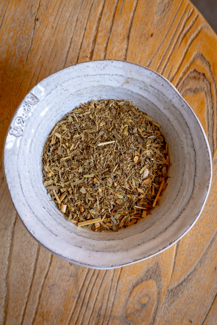 White bowl filled with dried herbs on a wooden surface