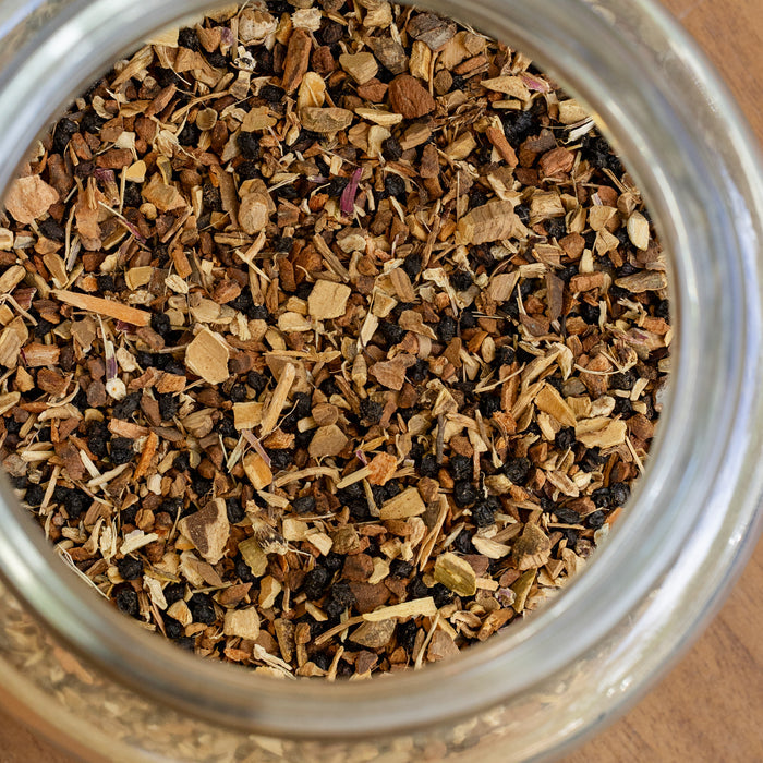 Close-up of a glass jar filled with dried herbs and spices on a wooden surface.