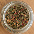 Clear glass jar filled with dried herbs on a wooden surface