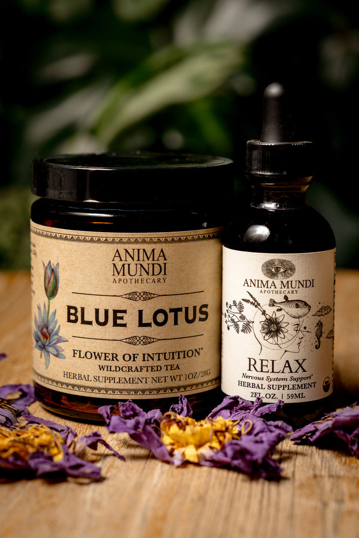 Two Anima Mundi products, a jar labeled 'Blue Lotus' and a bottle labeled 'Relax', on a wooden surface with dried flowers.