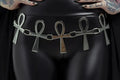 Model wearing a black outfit with a silver belt featuring ankh symbols on a plain background