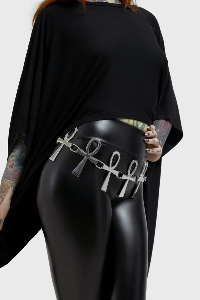 Model wearing a black outfit with a silver belt featuring ankh symbols on a plain background