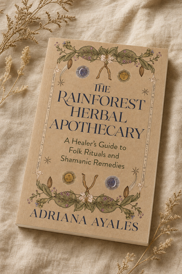 The Rainforest Herbal Apothecary book by Adriana Ayales, featuring a beige cover with botanical illustrations and dark blue text, styled on a textured beige linen fabric with dried flowers.