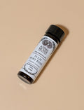 Small bottle of Tuisi Holy Basil oil with a black cap on a beige background